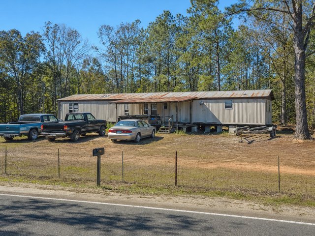 Generated image of a rural lot with a single-wide trailer, two pickups, a sedan and a boat trailer in a dirt yard